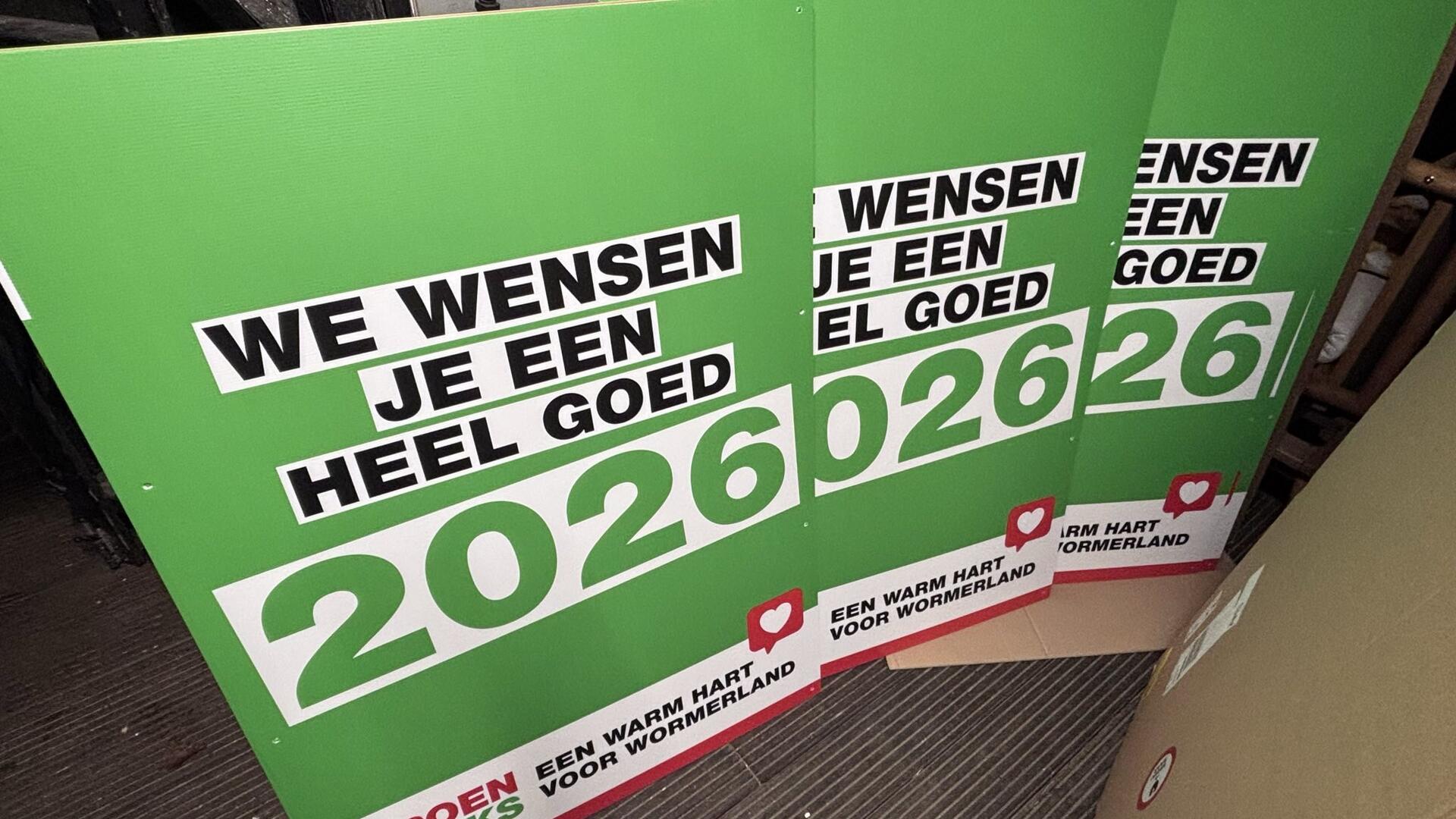 sandwichborden met tekst 'we wensen je een heel goed 2026' op groene achtergrond met wit hartje in rode like button. Daaronder nog de tekst 'Een warm hart voor Wormerland' en GroenLinks
